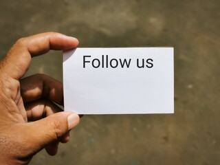 Selective focus image with noise effect hand holding white card with text FOLLOW US.Business concept.