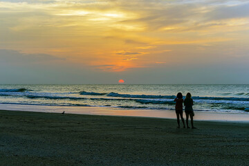 Silhouettes of couple of women gazing the orange sunrise on the horizon.