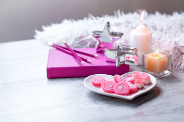 Sweet jelly in heart shaped plate for Valentine's day, with candle, silver star, pink book and white fur on wooden background