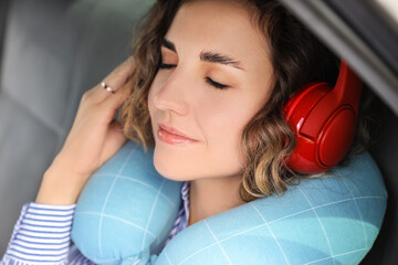 Beautiful young woman with travel pillow and headphones sleeping in car