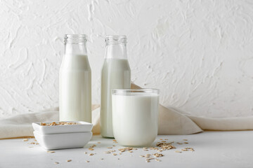 Bottles and glass of oat milk on light background