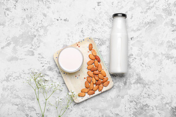 Bottle and glass of almond milk on light background