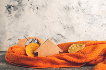 Figure of house, autumn leaves, piggy bank and warm scarf on grey background. Concept of heating season