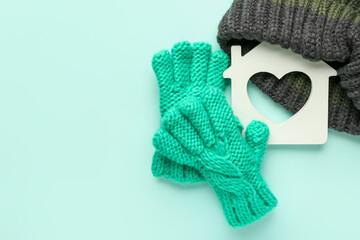 Figure of house and warm clothes on color background. Concept of heating season