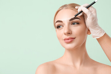 Young woman undergoing eyebrow correction procedure on color background