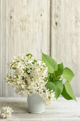 Bouquet of white spring flowers of lilac in a ceramic vase on a light wooden background. Festive interior decoration. Soft focus