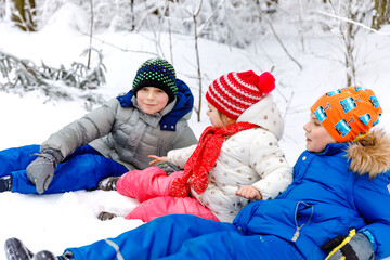 Two school kid boy and little toddler girl in winter forest. Happy children having fun with snow outdoors in winter. Family, three siblings, sister and brothers together, outdoors. Active leisure