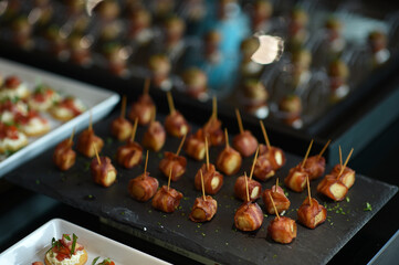 Close-up many pieces of small smoky cocktail sausages wrapped in grilled bacon and secure with a toothpick placed on the stone tray, appetizers on the buffet table for event party or in restaurant