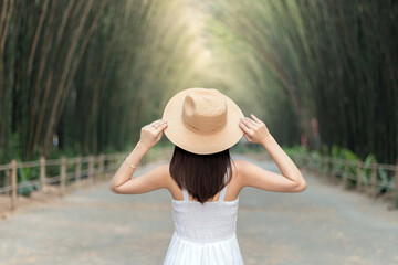 Back view beautiful woman  catch straw hat Walking and relaxing in the bamboo forest.