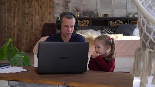 Remote work with a small child in home office during Covid-19 lockdown. Stressful dad is working on a laptop, baby girl is crying and acting up. Online virtual business video chat conference