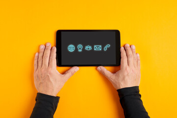 Male hand holding a black digital tablet displaying contact and communication icons