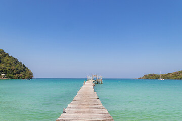 Fototapeta premium wooden bridge extended into the tropical seascape with beautiful clear blue sky.