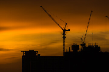 Silhouette building crane and buildings under construction against evening sky.