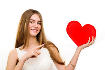 Portrait of smiling girl holding red heart and points finger at heart isolated on white background, valentine concept