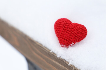Valentine heart in a snow on wooden bench. Red knitted symbol of love, background for winter holiday	