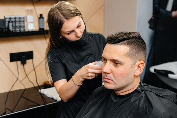 A professional stylist in a modern stylish barbershop shaves and cuts a young man's hair. Beauty salon, hair salon