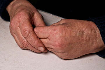 Senior woman's folded hands lie on the table. Wrinkles on the hands. Loneliness of the elderly.