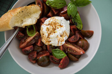 Caprese Tomaten Mozzarella Salat mit gestreiften bunten Tiger Tomaten in Schale mit Basilikum mit  Kräuterbaguette auf Hintergrund Mint Grün