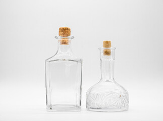 Empty glass carafe and empty glass bottle closed with cork caps isolated on a white background. Pair of the transparent bottles. Front view of the two vertical staying jars with different shape.