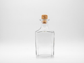 Empty glass bottle closed with cork cap isolated on a white background. Transparent square bottle. Front view of the vertical staying jar.