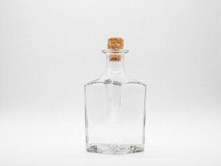 Empty glass bottle closed with cork cap isolated on a white background. Transparent square bottle. Front view of the vertical staying jar.