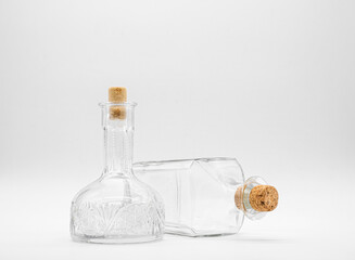 Upright empty glass carafe and empty glass bottle lying on its side closed with cork caps isolated on a white background. Pair of the transparent bottles with different shape.