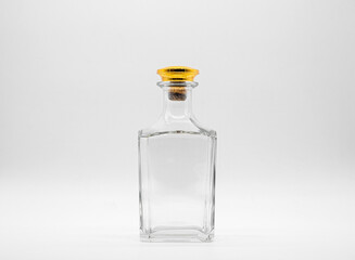 Empty glass bottle closed with big golden round cork isolated on a white background. Transparent square bottle. Front view of the vertical staying jar.