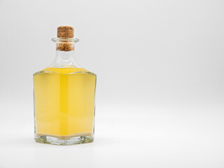 Glass bottle with alcohol drink closed with cork cap isolated on a white background. Transparent square bottle with yellow liquid. Front view of the vertical staying jar.
