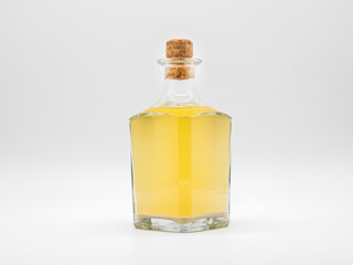 Glass bottle with alcohol drink closed with cork cap isolated on a white background. Transparent square bottle with yellow liquid. Front view of the vertical staying jar.