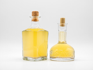 Alcohol drink in glass carafe and glass bottle closed with cork caps isolated on a white background. Pair of the transparent bottles with yellow liquid. Two vertical jars with different shape.