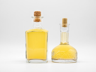 Alcohol drink in glass carafe and glass bottle closed with cork caps isolated on a white background. Pair of the transparent bottles with yellow liquid. Two vertical jars with different shape.