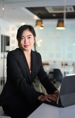 Portrait of businesswoman working with tablet computer and looking at camera while sitting at workspace.