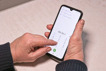 Elderly woman clicks a phone number on a smartphone. Hands of an old man.