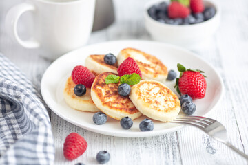 Cottage cheese pancakes with fresh berries on white wooden table. Tasty breakfast food. Syrniki - Image