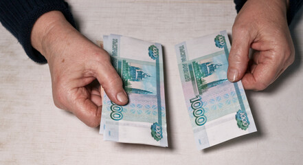An elderly woman is counting thousand-ruble banknotes. Old woman's hands and money. Old age, retirement savings and investment concept.