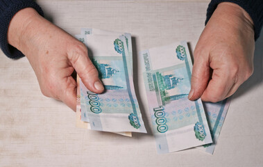 An elderly woman is counting thousand-ruble banknotes. Old woman's hands and money. Old age, retirement savings and investment concept.