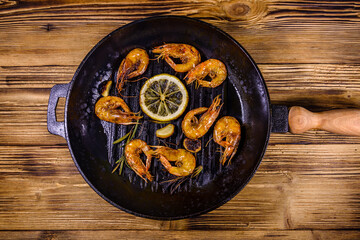 Roasted shrimps with lemon slice, garlic and rosemary in a cast iron pan. Top view
