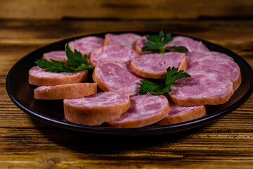 Black plate with sliced sausage on a wooden table