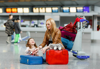 Cute little girl and mother at the airport. Tired family sitting on ground and waiting for delayed...