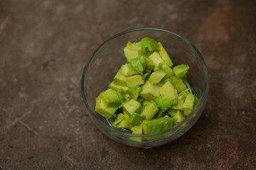 Ripe juicy diced avacado in a transparent bowl on a granite table.