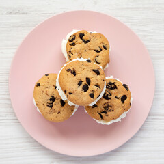 Homemade Chocolate Chip Cookie Ice Cream Sandwich on a pink plate on a white wooden surface, top view. Overhead, from above, flat lay.