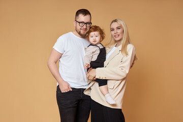 Happy family. Portrait of Mom, dad and daughter on a beige background. Beautiful couple in love holding their little daughter in their arms