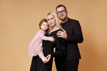 Happy family. Portrait of Mom, dad and daughter on a beige background. Beautiful couple in love holding their little daughter in their arms