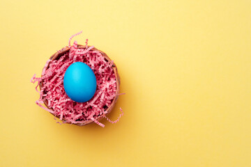 Blue Easter egg in a nest on yellow background