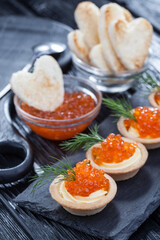 tartlets with butter and red caviar and dill on a black wooden table.
