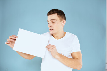 a man in a white t-shirt holds a sheet of paper copy space