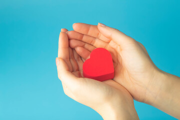 Heart in the hands of a female on a colored background. Donation, charity, health treatment, help concept. Background for Valentine's Day (February 14) and love.