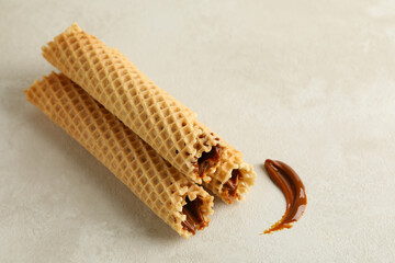 Tasty wafer rolls with condensed milk on white textured background