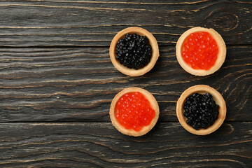 Tartlets with red and black caviar on wooden background, space for text
