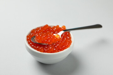 Bowl and spoon with caviar on gray background